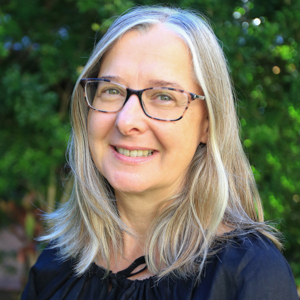 Women with Ash hair wearing glasses and dark shirt standing in front of trees