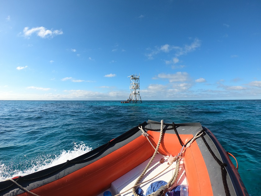Small boat in foreground with tall metal structure on reef