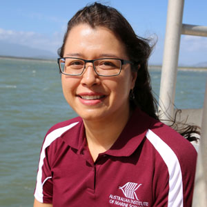 Brown haired woman with glasses wearing maroon shirt standing in front of ocean