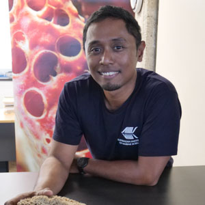 Man leaning on bench wearing navy blue shirt, standing in front of image of Coral