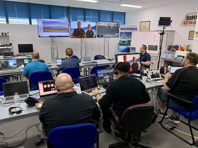 Inside the control room with people situated at many desks with many computers