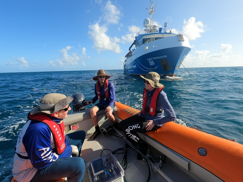 Group of scientists in a small boat infront of a large research vessel