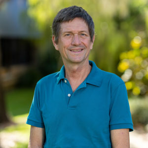 Man wearing blue shirt standing in front of green trees