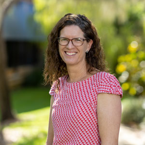 woman in red pattered shirt in front of trees, smiling