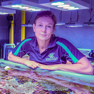 woman at aquaria tank filed with oral, standing under special aquaria lighting.