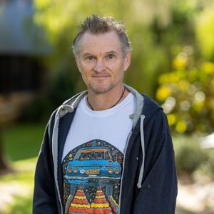 Man standing in a white T-shirt against a green background.