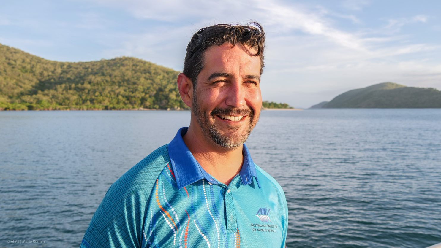 Dr Manuel Gonzalez Rivero wearing a blue shirt,  with the ocean and islands in the background.