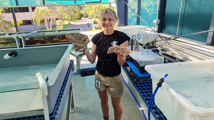 A woman stands among aquaria tubs with fragments of coral colonies in her hands.