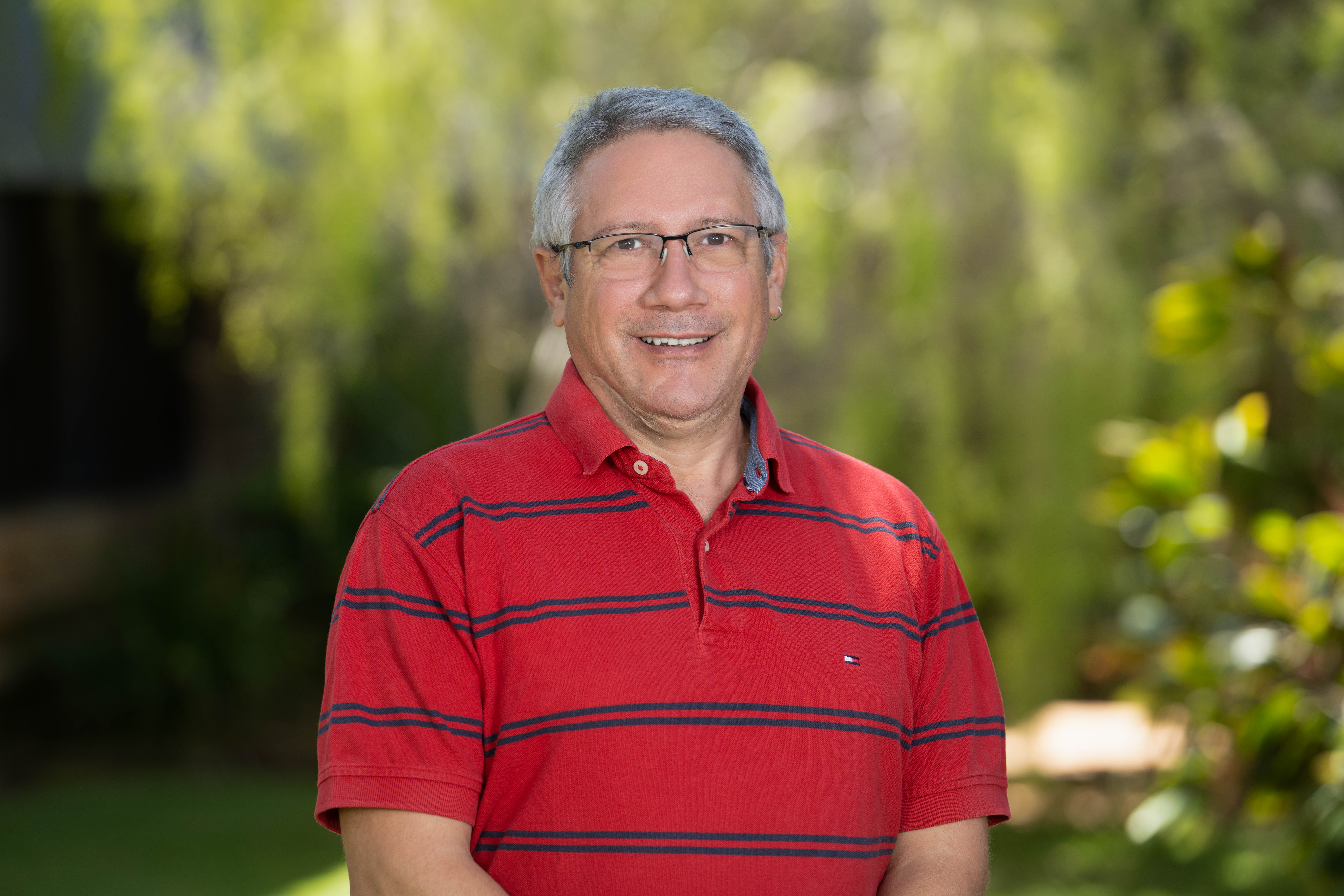 Hemerson Tonin standing in front of a leafy green background, wearing a red polo shirt.