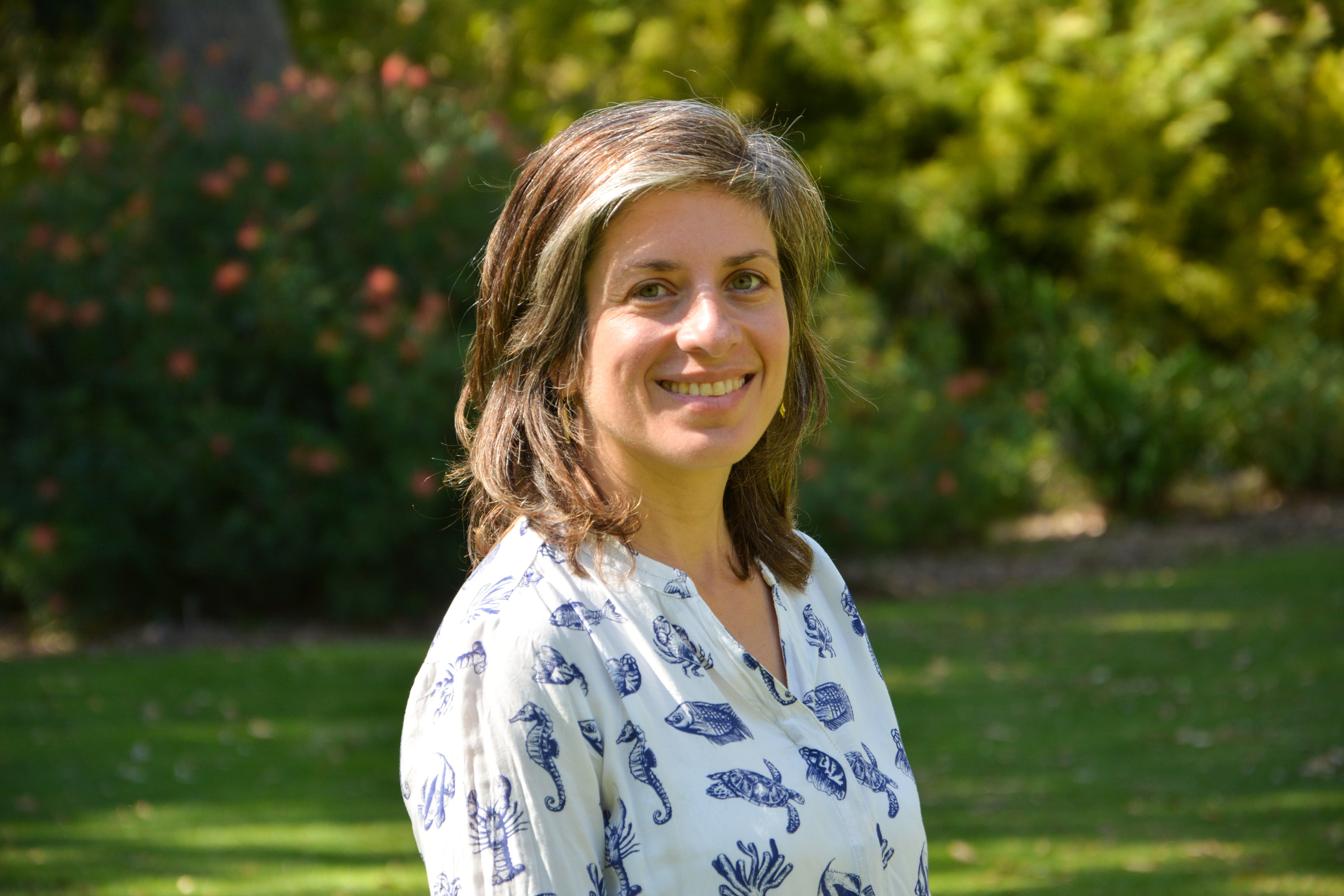 Katherine wearing a white blouse, smiling and standing in a grassy field.
