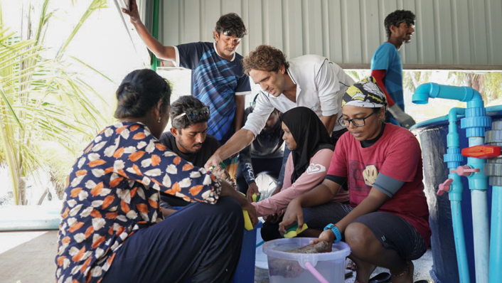 A group of people crowd around a small aquaculture tub