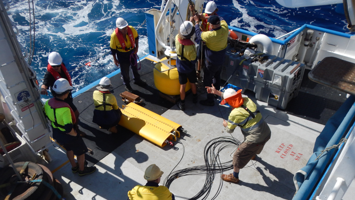 People deploy a high tech sensor from the back of a vessel