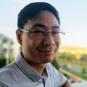 Dark haired man wearing glasses and, a blue and white check shirt