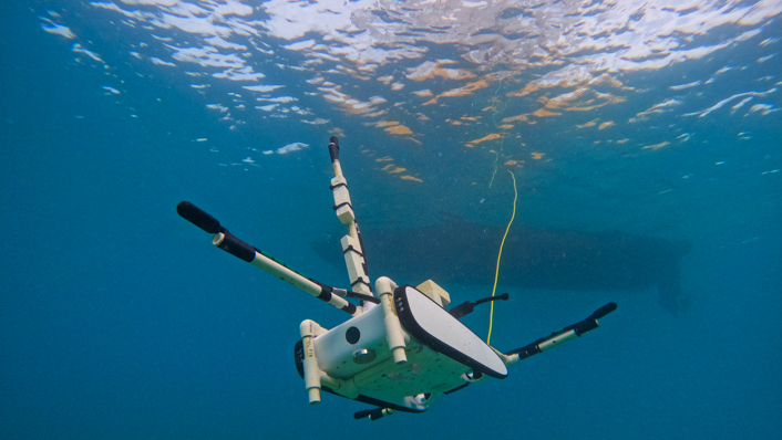 a remotely operated vehicle is underwater with a tether running to a boat at the surface