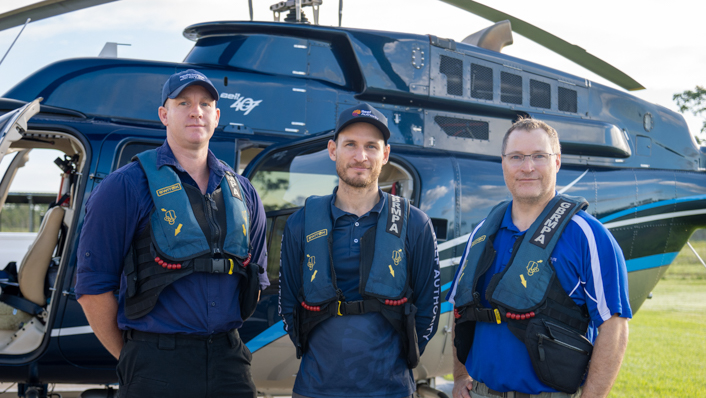 A group of men stand infront of a helicopter