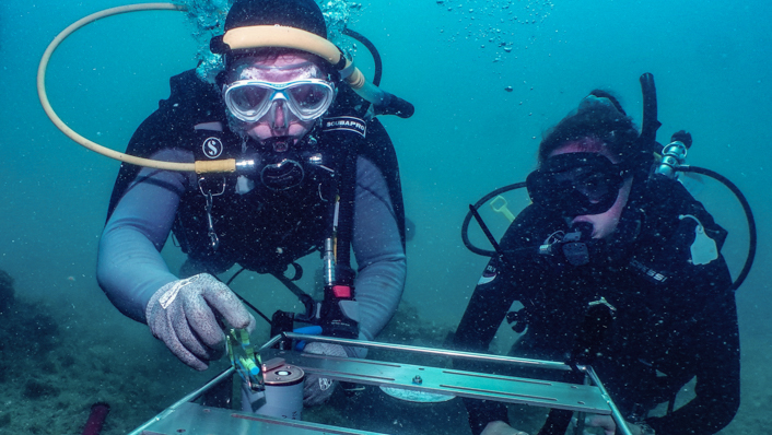 Two scuba divers are working with a metal instrument