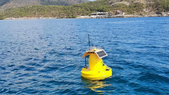 a large yellow buoy sits in calm water with a green hilly coastline in the distance