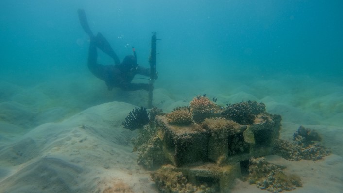 a person underwater working on equipment in front of a small patch reef