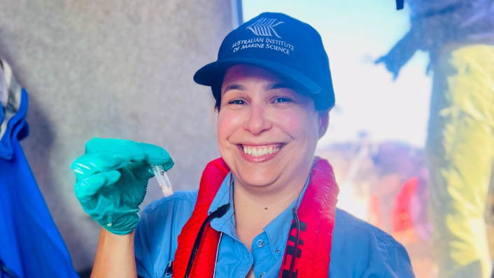 A woman in a cap smiles as she holds a sample in a small test tube