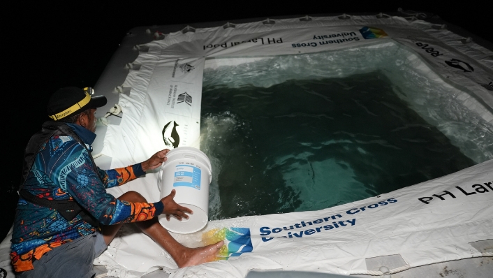 Scientist scooping water with bucket into an inflatable pool at night