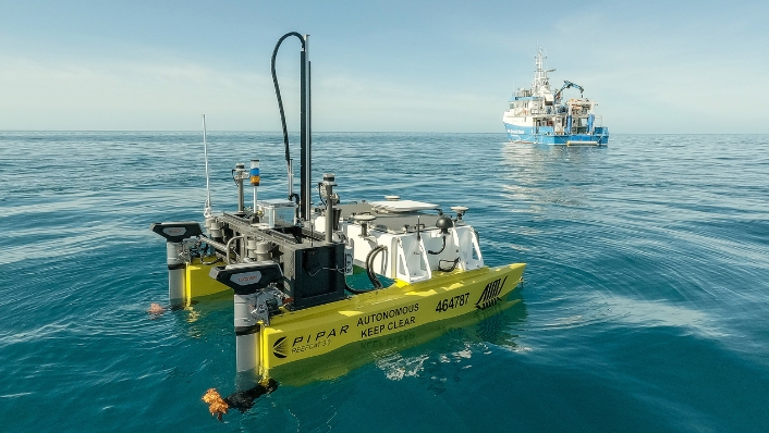ReefCat autonomous surface vehicle on the sea with research ship in background