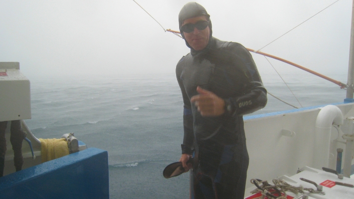 Marine scientist in wetsuit in the rain on a boat