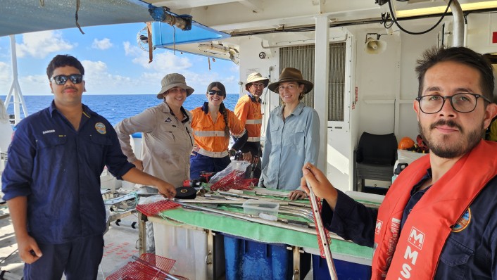 A group of people at a variety of distances from the camera pose for a picture around a work bench on a boat