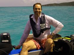 Man wearing life vest and long-sleeved shirt sitting in small boat with Ocean and Island in the background