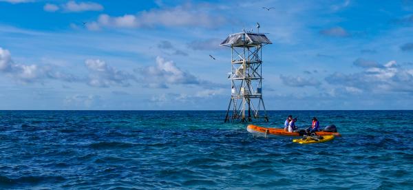metal tower sticking up out of the ocean with a small boat and people in front of the tower