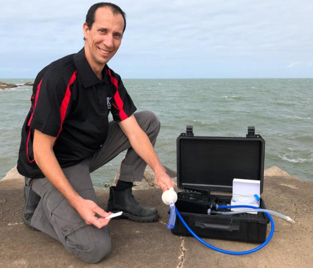 man kneeling next to box holding water sampling equipment and strip test.