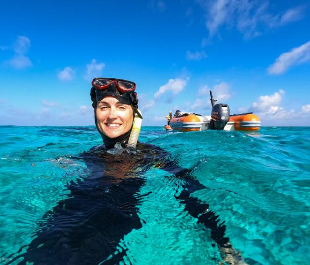 snorkeller in water smiling at camera with small bots in background