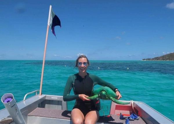 woman scientist on small vessel holding model of sea turtle