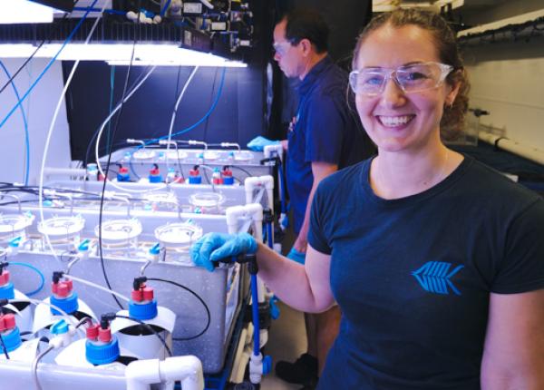 a sciencts in safety glasses and gloves stands next to an aquarium tank with glass jars inside