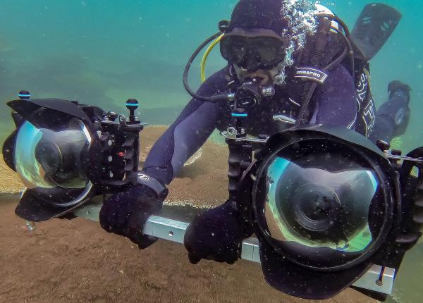 Scuba diver holds a bar with two large cameras on either end