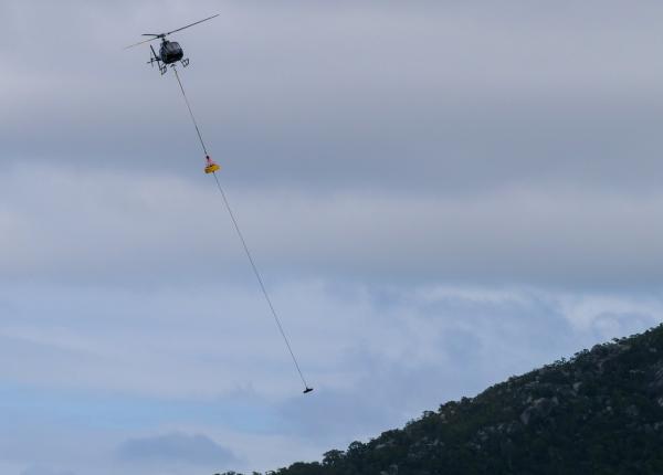 helicopter flies over a mountain with a cargo load hanging underneath