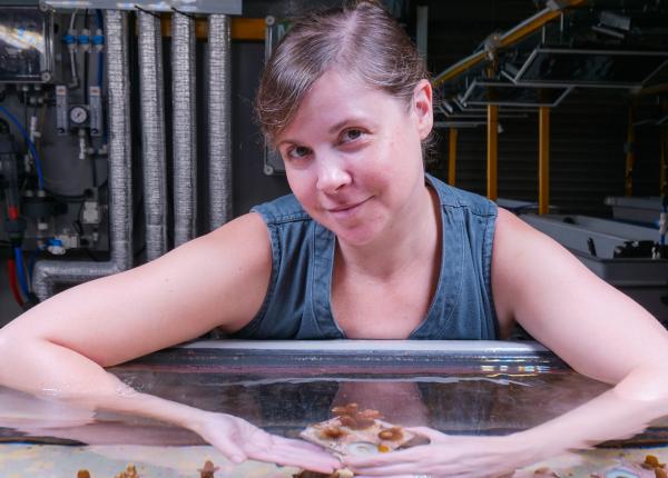 A woman is in an aquaria facility holding a small tray of coral fragments