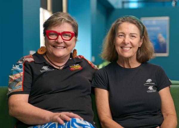 two women sitting on a couch together and smiling at the camera