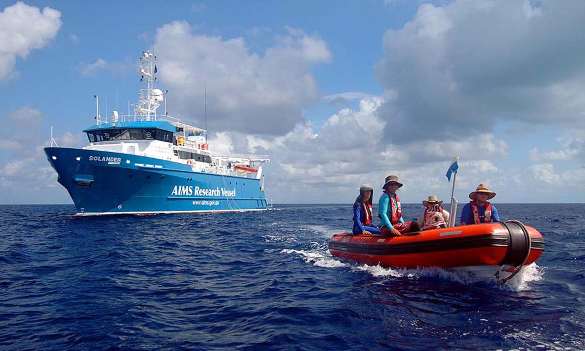 small orange vessel departing large research vessel with people