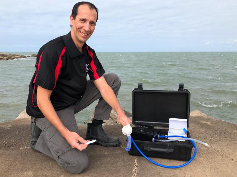man kneeling next to box holding water sampling equipment and strip test.