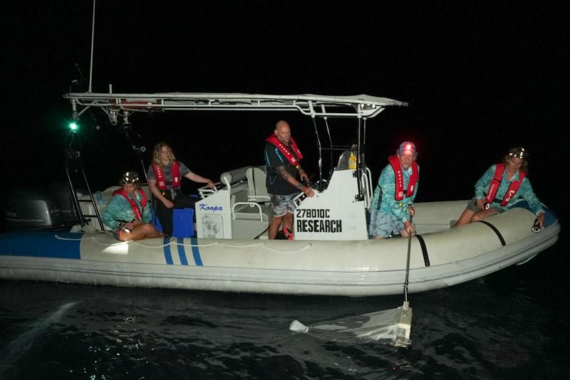 People on small vessel at night with small net in water