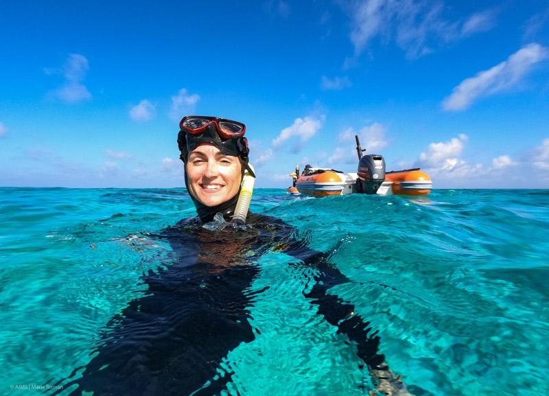 snorkeller in water smiling at camera with small bots in background