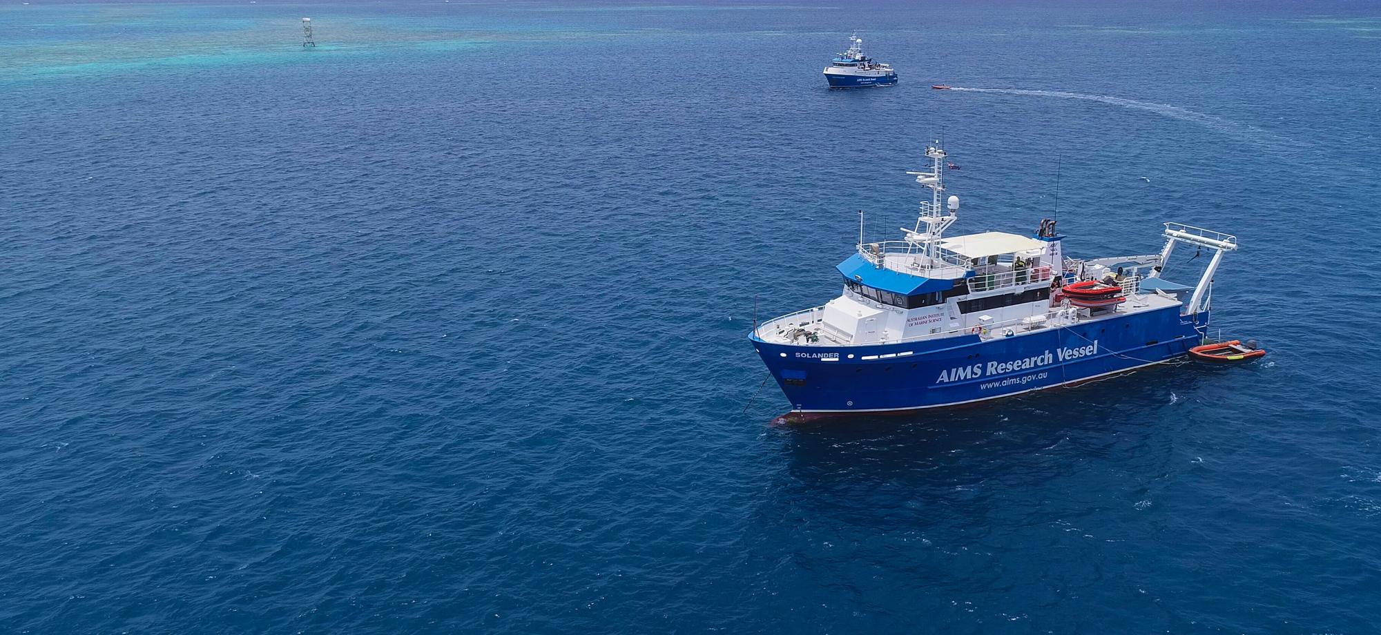 blue and white AIMS vessels on the reef on a calm day, photo taken from the air