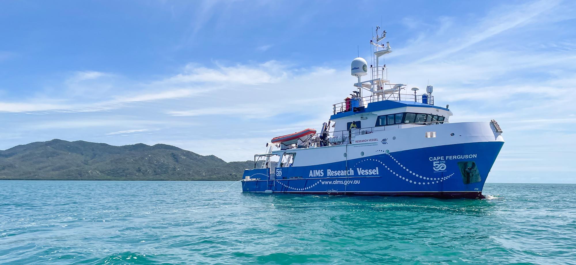 blue and white research vessel on a calm sea with island in background