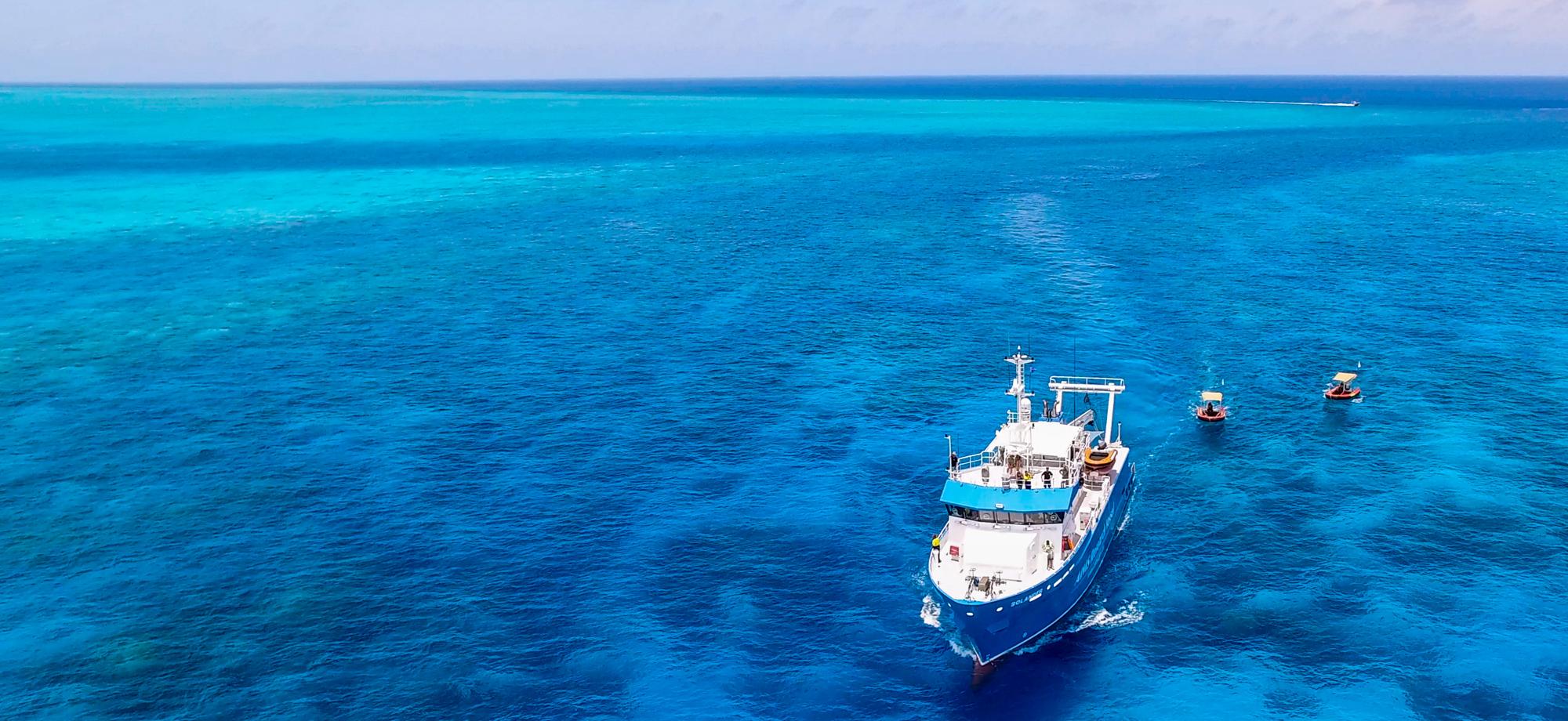 blue and white research vessel and orange tender on calm reef
