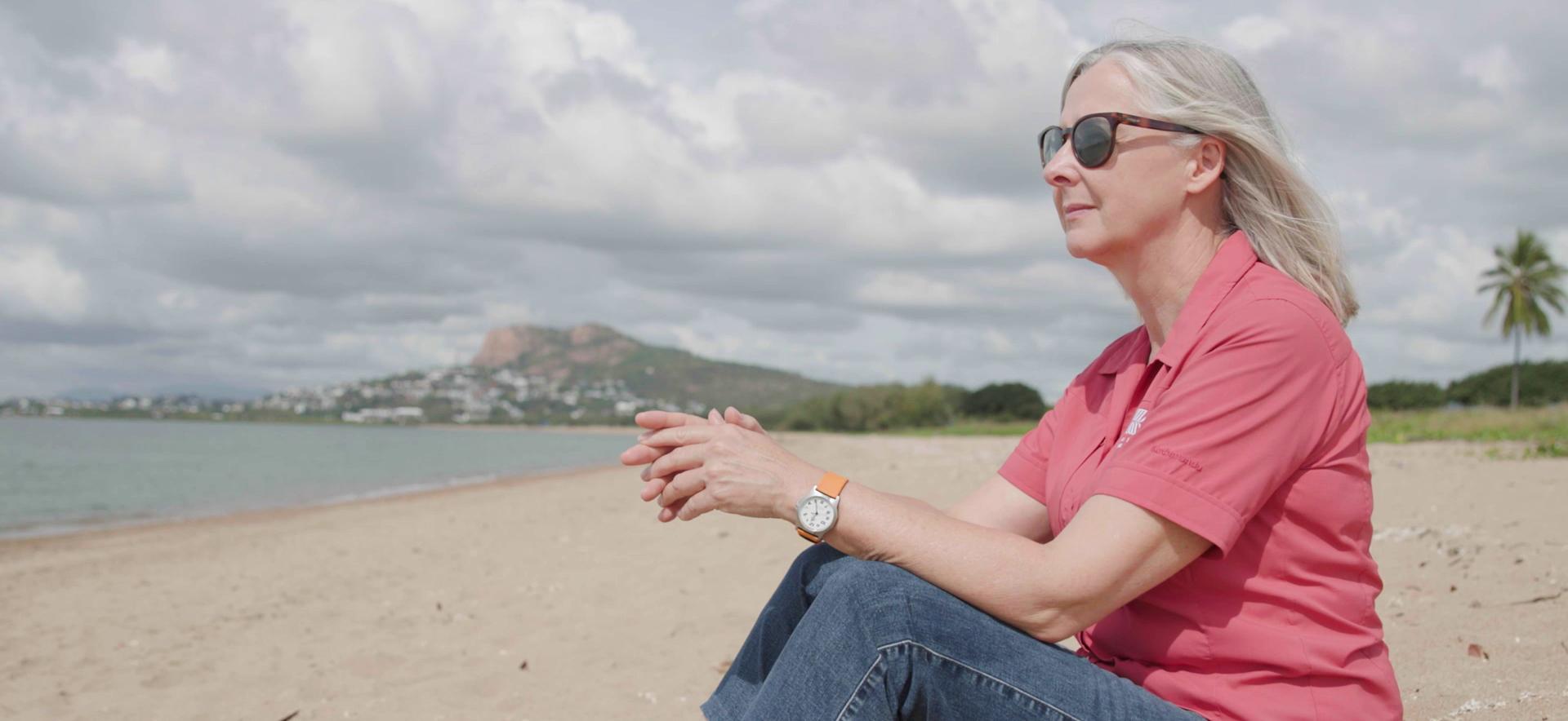 marine scientist sits on a beach with castle hill in townsville in the background
