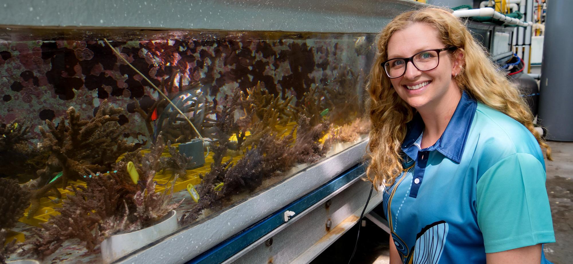 a person sitting next to an aquaria with sea creatures looks at the camera, smiling