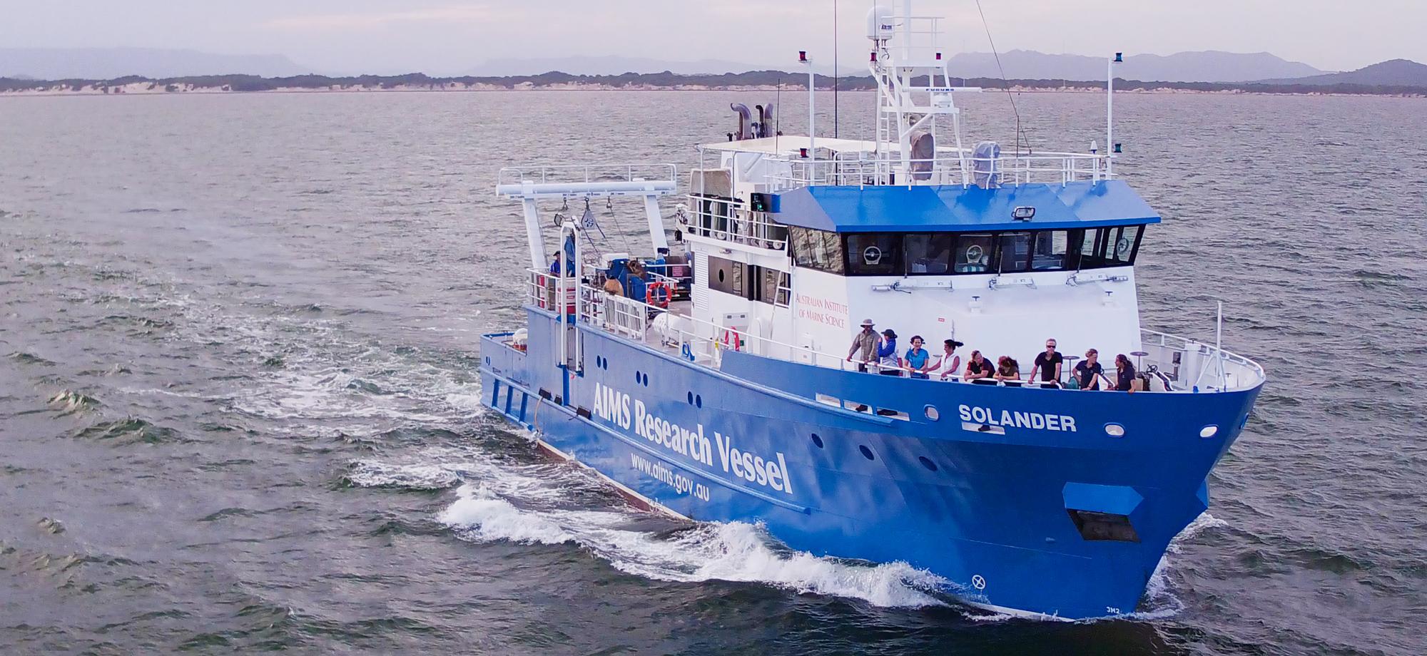 a blue and white research vessel with people standing near the bow looking out to sea