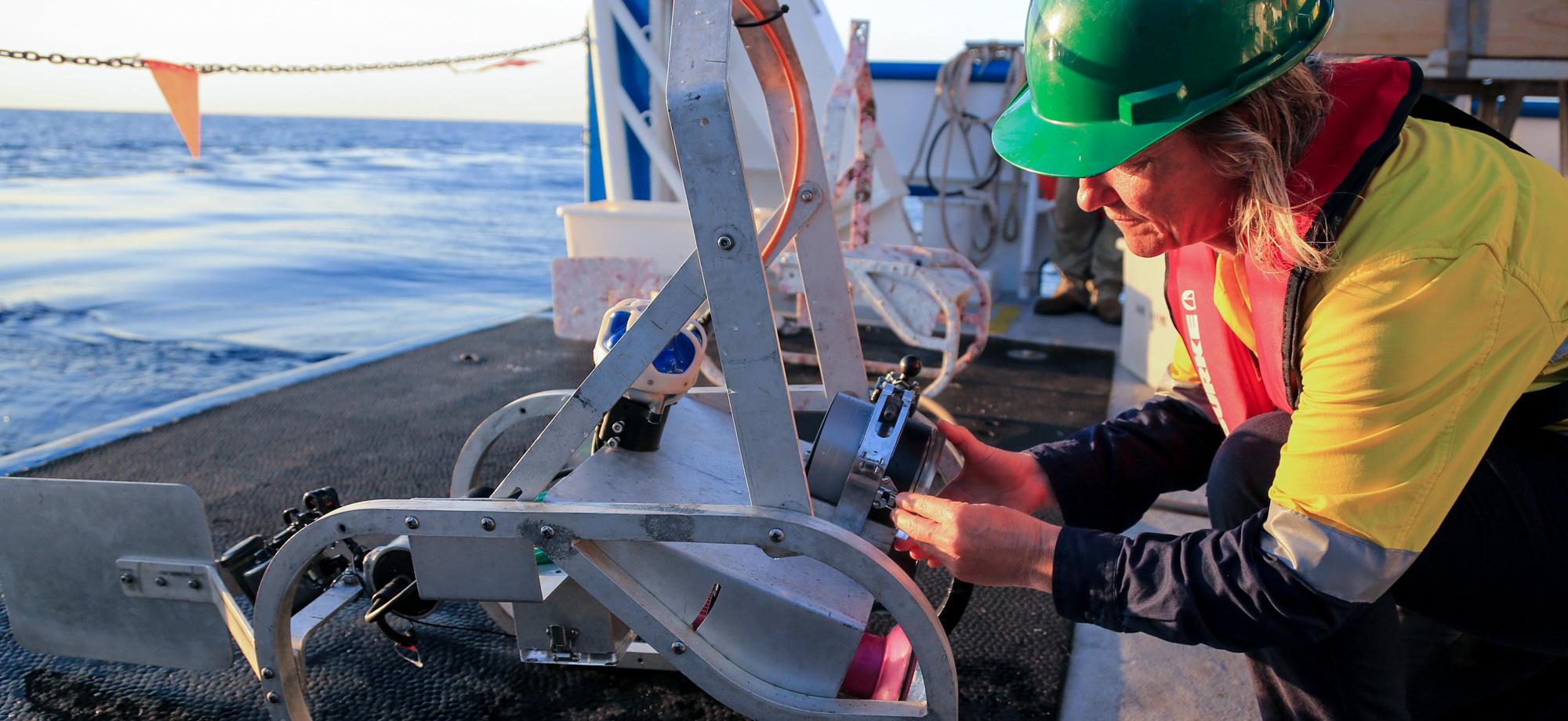 scientist in hi vis with towed camera on back deck of vessel
