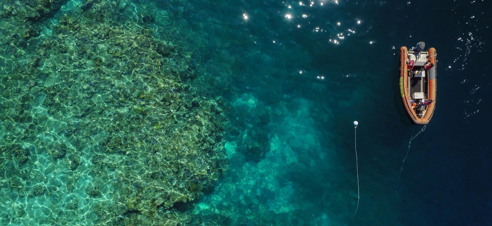aerial view of a reef with an orange inflatable tender moored next to it.