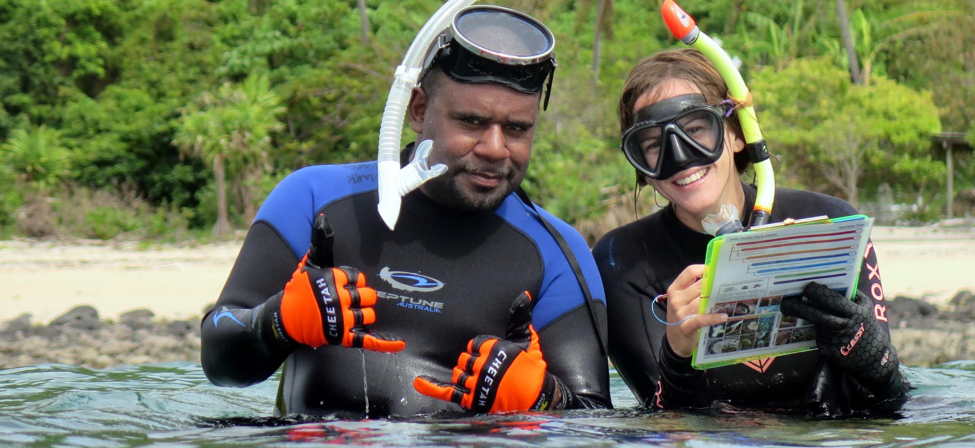 two snorkellers sit together in the water, looking at the camera and smiling